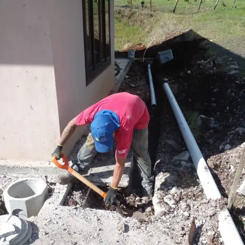 Técnico excavando la zanja para instalar tubería PVC junto a una vivienda
