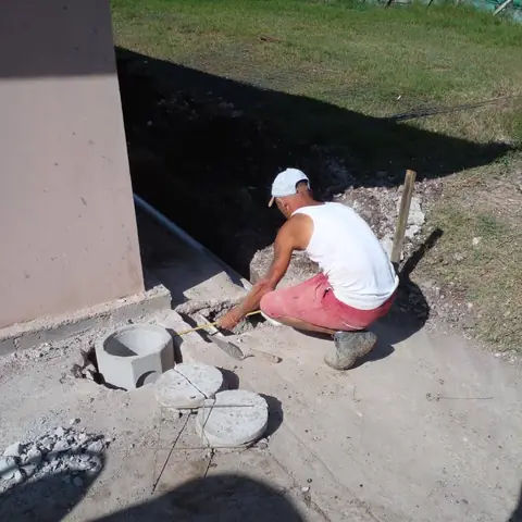 Técnico colocando cajas de registro de concreto junto a una vivienda