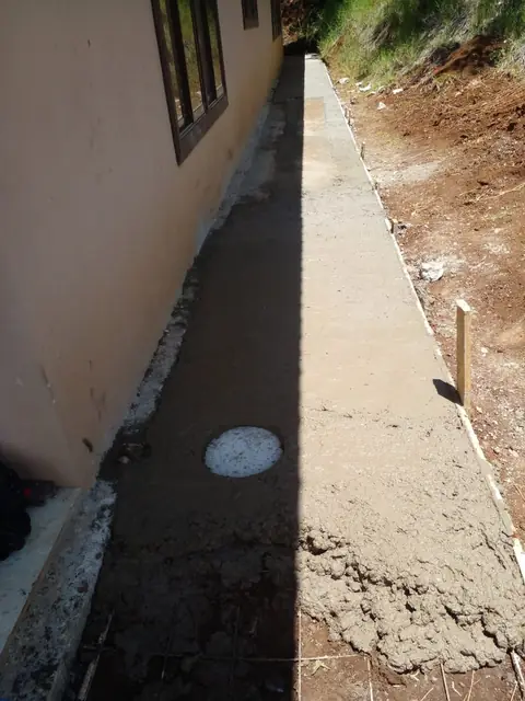 Contrapiso de concreto recién terminado con tapa de registro al costado de una casa